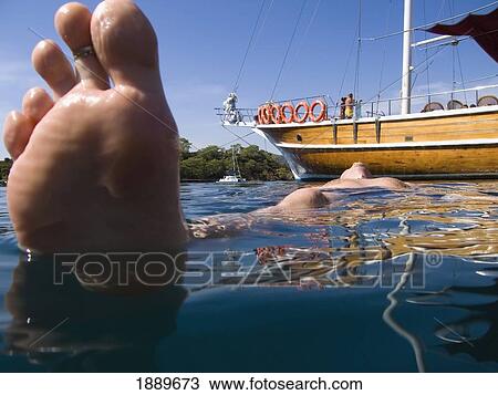 Stock Image - Male Swimmer Floating Alongside A Moored Boat, Low Angle View. Fotosearch
