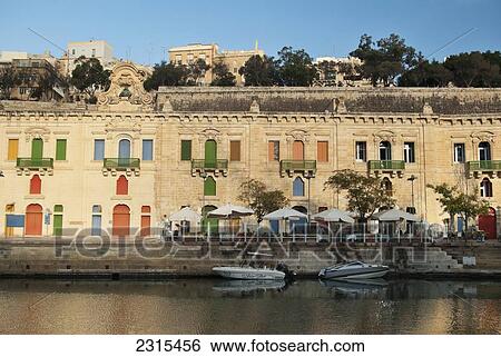 Stock Photograph - Malta, Valetta, View of Grand Harbor with restaurant and sandstone building in background. Fotosearch