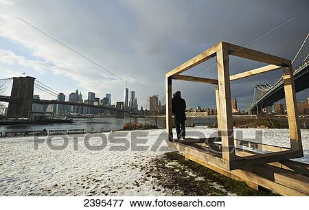 Stock Photo - Man and public sculpture in Brooklyn looking towards Manhattan; New York City, New York, United States of America. Fotosearch