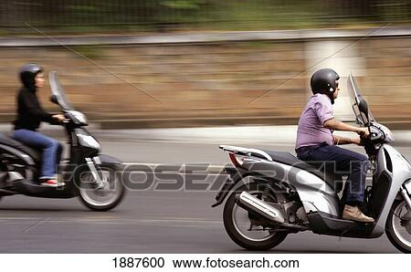 Stock Image - Man And Woman Riding Scooters, Blurred Motion. Fotosearch