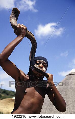 Stock Photograph - Man Blowing Into Horn Instrument, Shamwari. Fotosearch