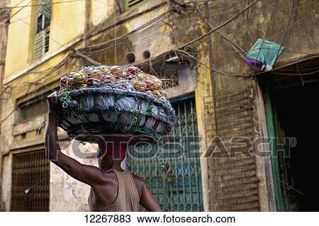 Stock Image - Man carrying fruit in a basket on his head; Kolkata, West Bengal, India. Fotosearch