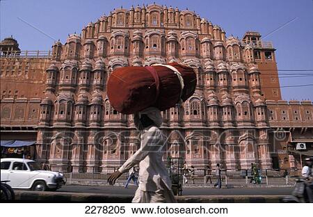 Stock Photography - Man carrying red bundle on head in front of Hawa Mahal, Palace Of The Winds; Jaipur, Rajasthan, India. Fotosearch