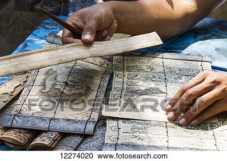 Stock Image - Man carving the ancient tales and the famous Ramayana story in Sanskrit on lontar leaves, Tenganan Pegringsingan, Bali, Indonesia. Fotosearch