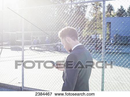 Man checking his cell phone by a schoolyard's chain link fence; British Columbia, Canada View Large Photo Image Stock Photo - Man checking his cell phone by a schoolyard's chain link fence; British Columbia, Canada. Fotosearch