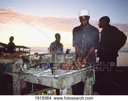 Picture - Man Cooking Kebabs In Sunset. Fotosearch