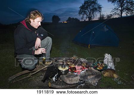Stock Photo - Man Cooking Over Charcoal Embers Of Wood Fire, Dartmoor National Park, Postbridge, Yelverton, Devon, Uk. Fotosearch