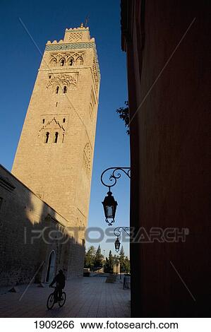 Stock Photograph - Man Cycling Beaneath Minaret Of Koutoubia Mosque At Dawn, Marrakesh, Morocco. Fotosearch