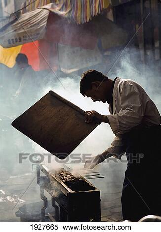 Stock Photography - Man Fanning Embers For Lamb Kebabs. Fotosearch