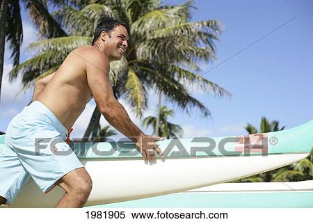 Stock Photography - Man holding front of outrigger canoe.. Fotosearch
