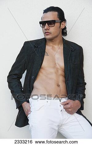 Stock Photograph - Man in a blazer and sunglasses, leaning against a white wall; Honolulu, Oahu, Hawaii, United States of America. Fotosearch