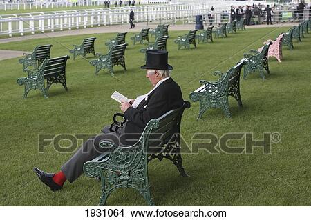 Picture - Man in a top hat and fashionable clothes sitting by the rails at new Grandstand Enclosure during Royal Ascot horse racing meeting. Berkshire. England., Berkshire. England.. Fotosearch