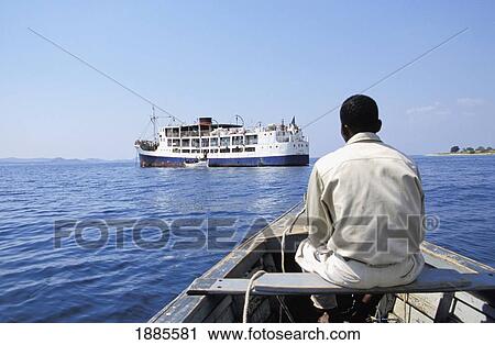 Stock Image - Man In Boat With Ilala Steamer In Background On Lake Nyasa. Fotosearch
