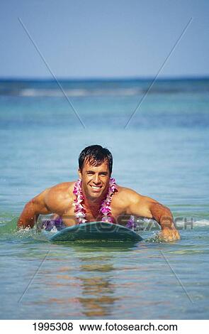 Stock Photo - Man In Ocean Paddling Toward Camera, Smiling And Wearing Orchid Lei. Fotosearch