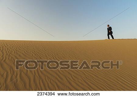 Man in smart suit walking along top of sand dune at dusk; Dubai, United Arab Emirates View Large Photo Image Picture - Man in smart suit walking along top of sand dune at dusk; Dubai, United Arab Emirates. Fotosearch