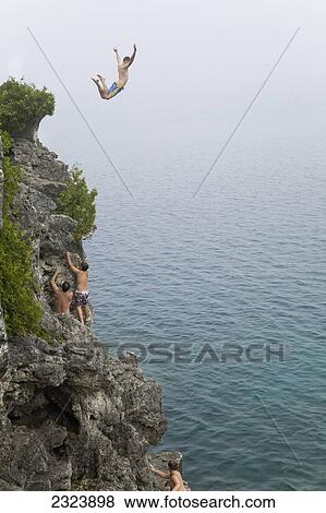 Stock Photo - Man leaping from a cliff into turquoise water of Georgian Bay in Bruce Peninsula National Park; Ontario, Canada. Fotosearch