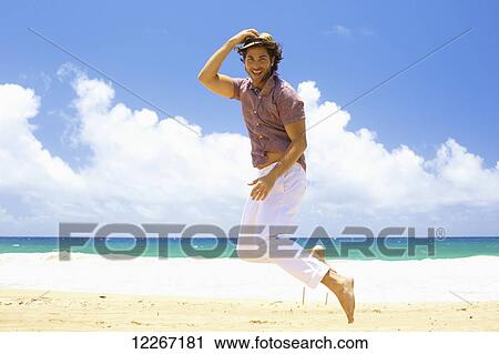 Stock Image - Man leaping in the air on the beach; Kealia, Kauai, Hawaii, United States of America. Fotosearch