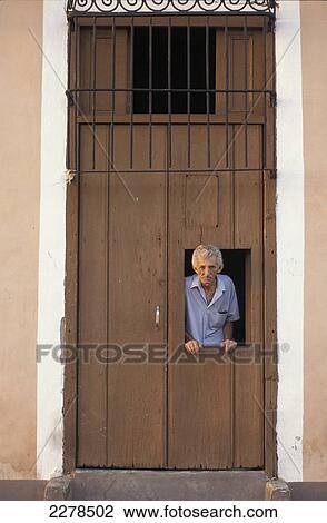 Stock Image - Man looking out window of wooden door; Trinidad, Cuba. Fotosearch