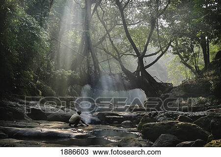 Stock Image - Man Making Fire Beside River And Natural Footbridge. Fotosearch