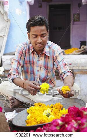 Stock Image - Man making maragold garland blue town in Jodphur Rajasthan India. Fotosearch