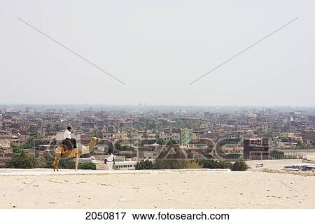 Stock Photo - Man On A Camel And Skyline Of Cairo, As Seen From Giza, Al Jizah, Egypt. Fotosearch