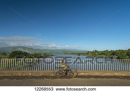 Stock Image - Man on bicycle crossing bridge over the Shire River, near Chikwawa; Malawi. Fotosearch