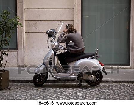 Stock Photograph - Man On The Phone Sitting In Scooter; Rome, Italy. Fotosearch