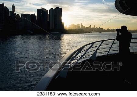 Stock Image - Man onboard a cruise ship taking photographs of New York skyline in the early morning; New York City, New York, United States of America. Fotosearch