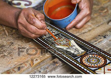 Stock Photography - Man painting a traditional Toraja design on piece of wood, Kete Kesu, Toraja Land, South Sulawesi, Indonesia. Fotosearch