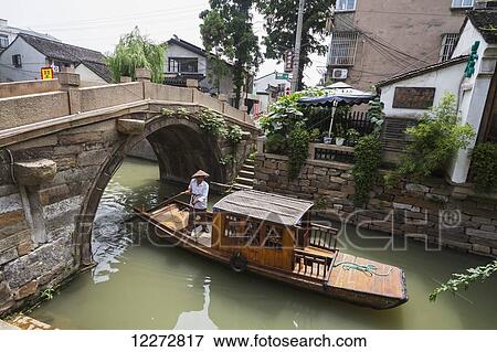Stock Photo - Man punting a boat by a bridge over the North-South canal by Pingjiang Road, Suzhou, Jiangsu, China. Fotosearch