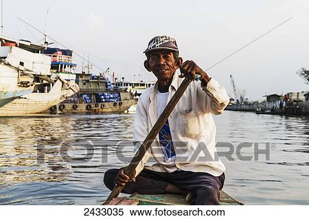 Stock Photography - Man rowing a boat in Sunda Kelapa Harbour, Jakarta, Java, Indonesia. Fotosearch