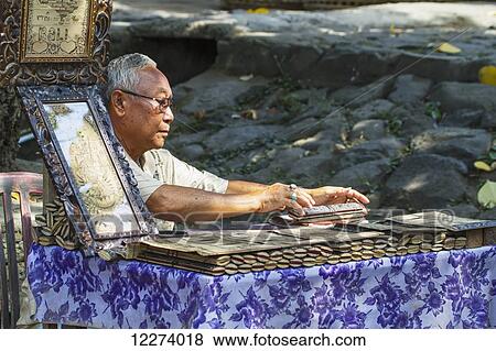Man selling carvings of the ancient tales and the Ramayana epic in Sanskrit on lontar leaves, Tenganan Pegringsingan, Bali, Indonesia View Large Photo Image Stock Photo - Man selling carvings of the ancient tales and the Ramayana epic in Sanskrit on lontar leaves, Tenganan Pegringsingan, Bali, Indonesia. Fotosearch