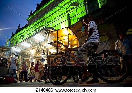 Stock Photograph - Man Selling Popcorn And Kid On A Bike In Front Of Teatro Guarany At Night, Pelotas, Rio Grande Do Sul, Pelotas, Brazil. Fotosearch