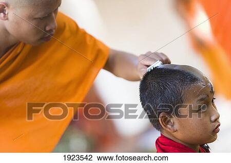Stock Image - Man Shaving Head Of Novice Monk At Wat Naluang, Luang Prabang, Northern Laos. Fotosearch