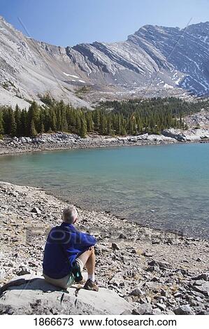 Stock Image - Man Sitting Beside A Mountain Lake. Fotosearch