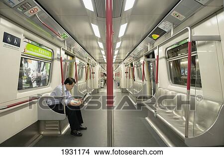 Picture - Man Sitting On An Empty Underground Subway Train Reading A Newspaper. Hong Kong; Hong Kong.. Fotosearch