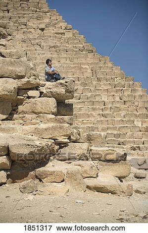 Stock Photo - Man Sitting On Part Of A Pyramid In The Desert. Fotosearch