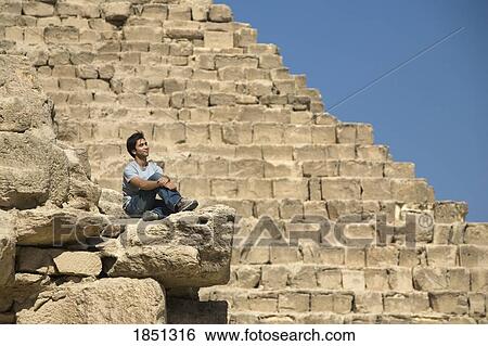 Stock Photograph - Man Sitting On Part Of A Pyramid In The Desert; Cairo, Egypt, Africa. Fotosearch