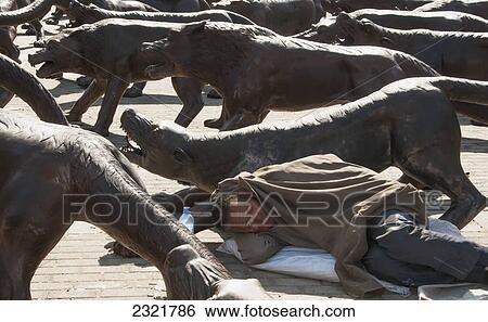 Stock Photograph - Man sleeping on ground beside statues of various wild animals; Beijing, China. Fotosearch