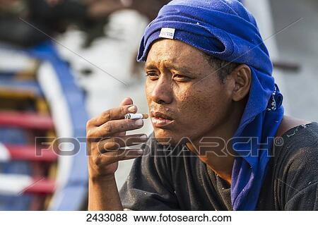 Stock Photo - Man smoking a cigarette in Sunda Kelapa Harbour, Jakarta, Java, Indonesia. Fotosearch