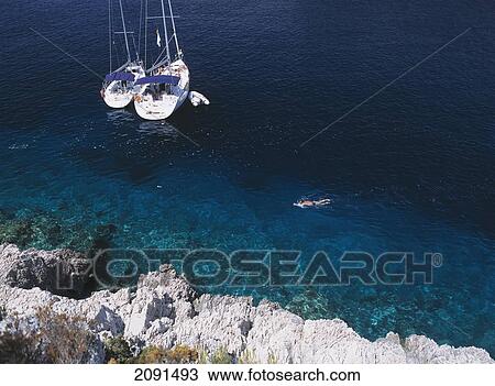 Stock Image - Man Snorkelling Past Two Yachts Moored In Small Bay On The Island Of Bisevo Off Vis, Croatia.. Fotosearch