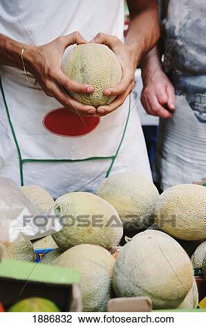 Stock Image - Man Squeezing A Melon To Check Ripeness. Fotosearch