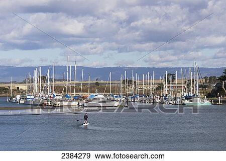 Stock Photo - Man stand up paddleboarding with boats in the harbour, Moss Landing; Monterey Bay, California, United States of America. Fotosearch