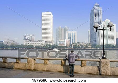 Stock Photograph - Man Standing By River With Guangzhou Business District In Background. Fotosearch
