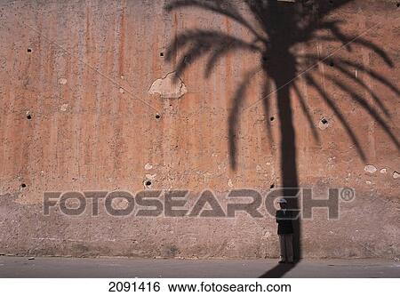Man Standing In Shadow Of Date Palm On The Old City Walls Of Marrakesh, Morocco. View Large Photo Image Stock Photograph - Man Standing In Shadow Of Date Palm On The Old City Walls Of Marrakesh, Morocco.. Fotosearch