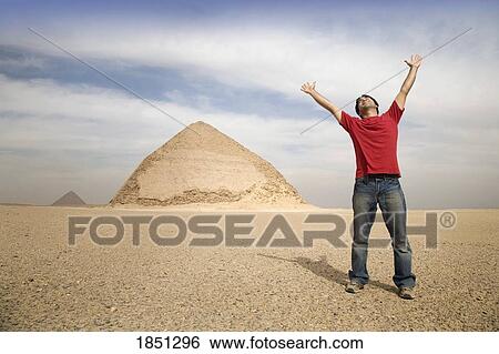 Stock Photograph - Man Standing Near The Pyramids With His Arms Up; Cairo, Egypt, Africa. Fotosearch