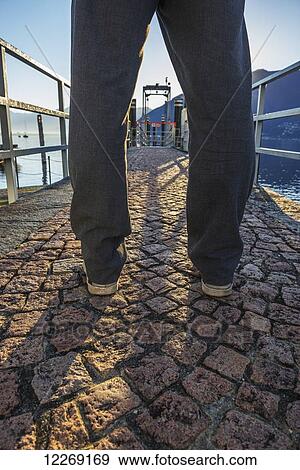 Stock Photo - Man standing on a stone walkway on the waterfront; Locarno, Ticino, Switzerland. Fotosearch