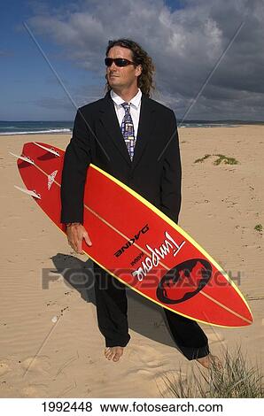 Man Standing On Beach In Business Suit Holding A Surfboard. View Large Photo Image Stock Photo - Man Standing On Beach In Business Suit Holding A Surfboard.. Fotosearch