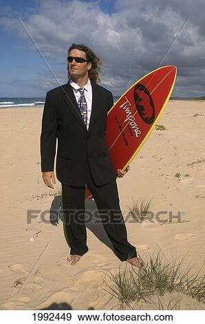 Man Standing On Beach In Business Suit Holding A Surfboard. View Large Photo Image Stock Photo - Man Standing On Beach In Business Suit Holding A Surfboard.. Fotosearch