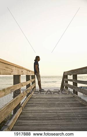 Stock Photo - Man Standing On Boardwalk At Ocean. Fotosearch